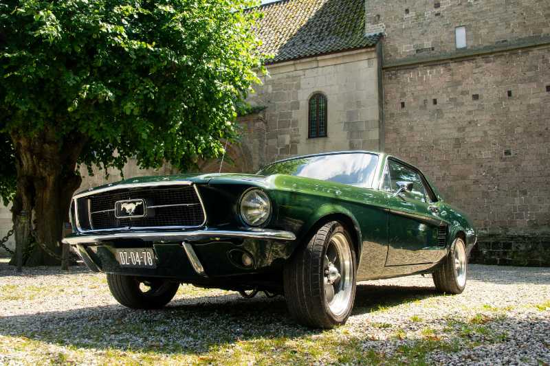 a green mustang parked in front of a brick building
