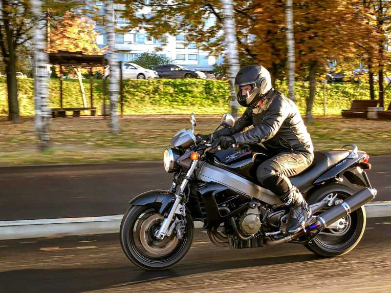 Un hombre con chaqueta negra conduciendo una motocicleta negra en la carretera