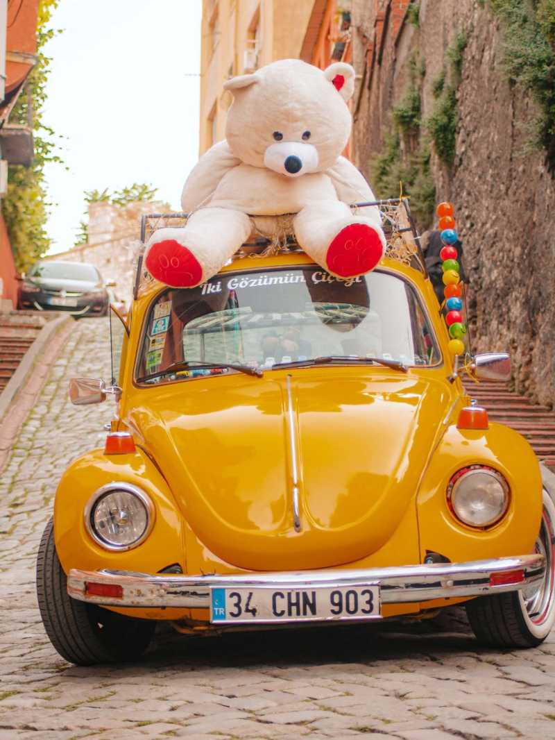 Ein gelbes Auto mit Teddybär auf dem Dach parkt auf der Straße