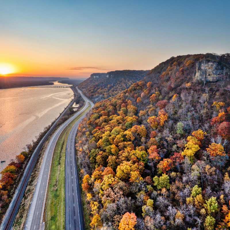 Aerial View of a Mountain Covered in Colorful Trees and a River at Sunset