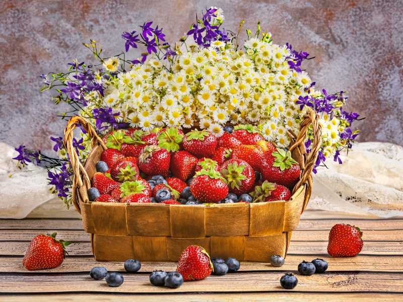 A basket with summer berries strawberries blueberries and a bouquet of wild flowers with daisies