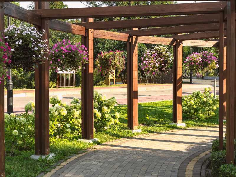 Beautiful alley in a summer park with blooming petunias and hydrangea flowers wooden archway paths