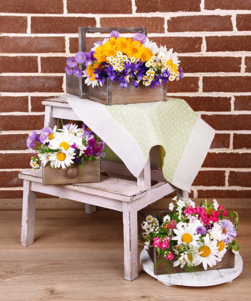 Beautiful flowers in crates on small ladder on brick wall background