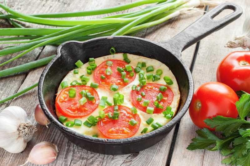 Sartén negra con huevos revueltos y tomates sobre una mesa rústica de madera
