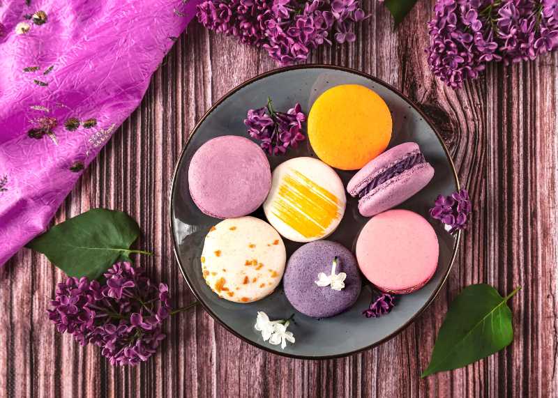Colorful macarons on a plate surrounded by vibrant purple lilac flowers