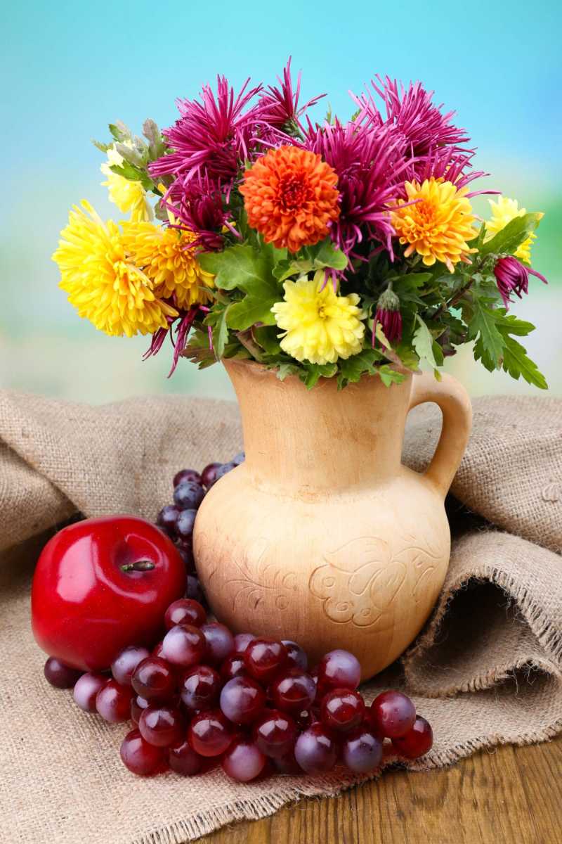 Composition with beautiful flowers in pitcher and fruits on bright background