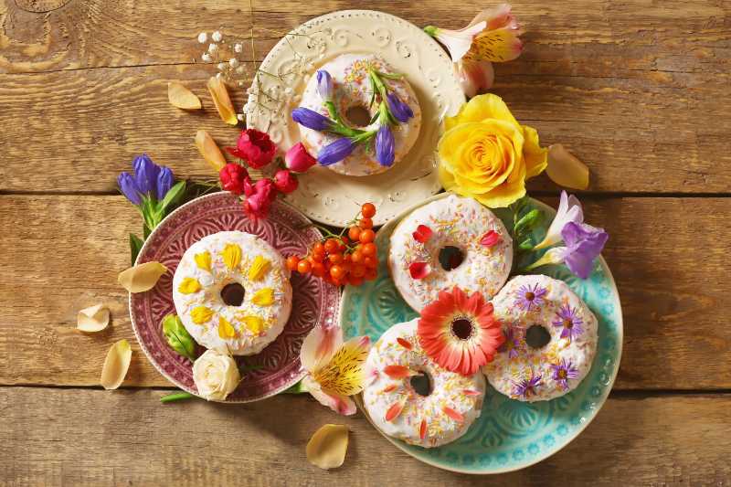 Composition of plates with delicious donuts and colourful flowers on wooden table