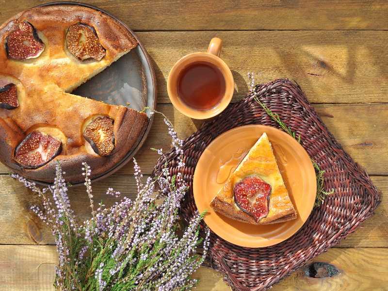Curd pudding with figs and honey on wicker brown napkin and herbal tea with heather on the wooden background

