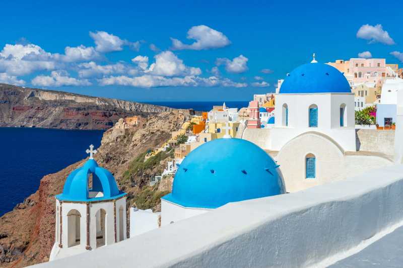 Capture the breathtaking scenery of Santorini's unique architecture and vibrant blue domes under a clear summer sky
