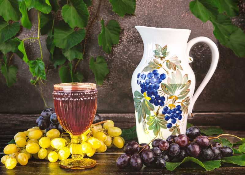 A glass of red wine grape branches on a wooden tray vintage jug grape leaves