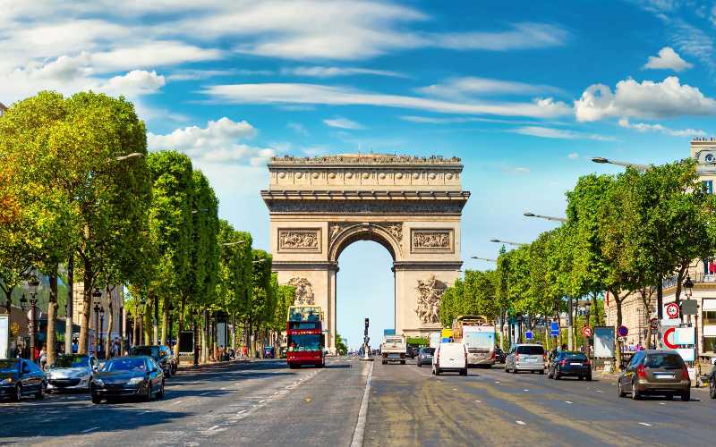 Iconic view of the Arc de Triomphe monument with busy traffic and trees in Paris