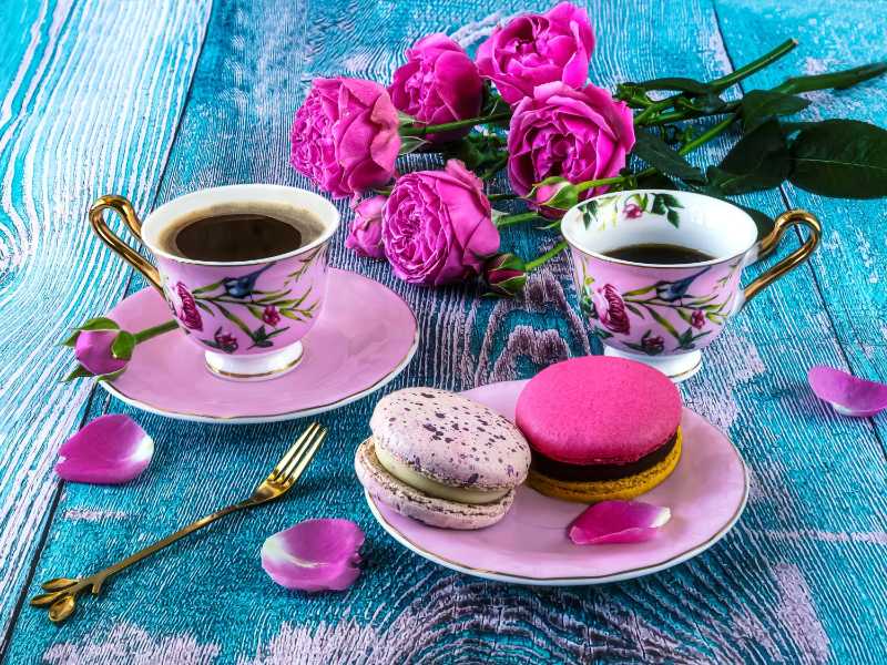Macaroons and two pink cups of coffee and blooming pink roses