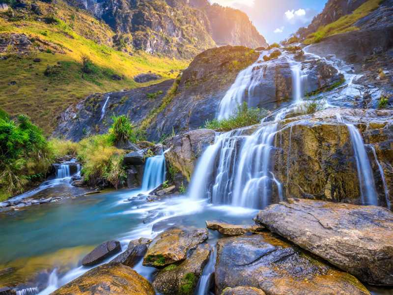 Majestic mountain waterfall cascading into a clear river with lush greenery