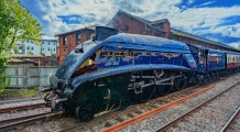 a blue train traveling down train tracks next to a building - jigsaw puzzle