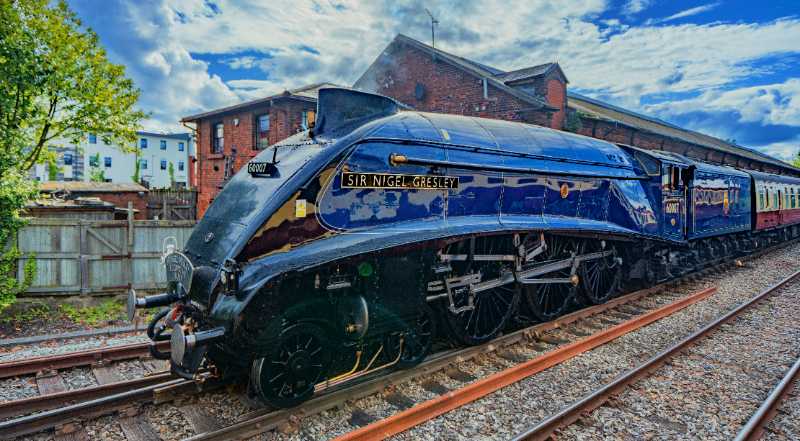 a blue train traveling down train tracks next to a building - jigsaw puzzle