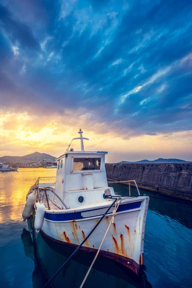 old fishing boat in port of naousa on sunset with dramatic sky paros lsland greece