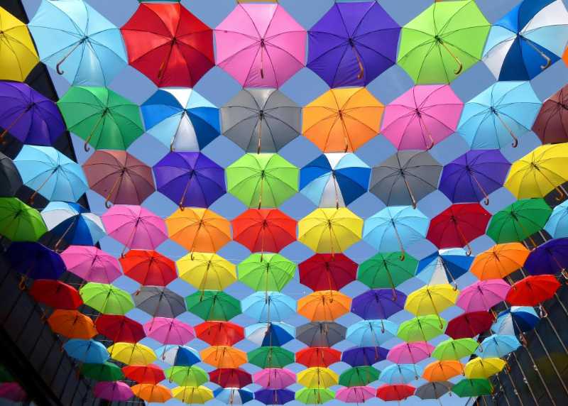 yellow blue red pink purple green multicolored open umbrellas hanging on strings under blue sky - jigsaw puzzle