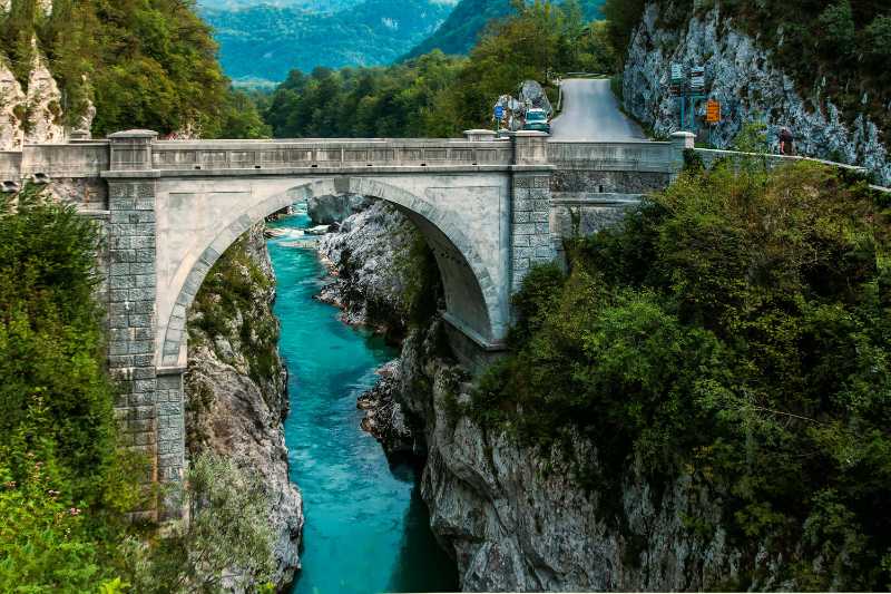 concrete bridge over clear blue river beside mountain - jigsaw puzzle