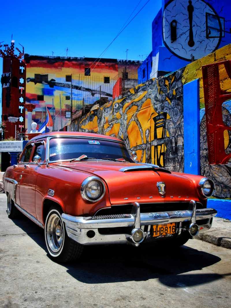 Red vintage car parked beside a graffiti wall