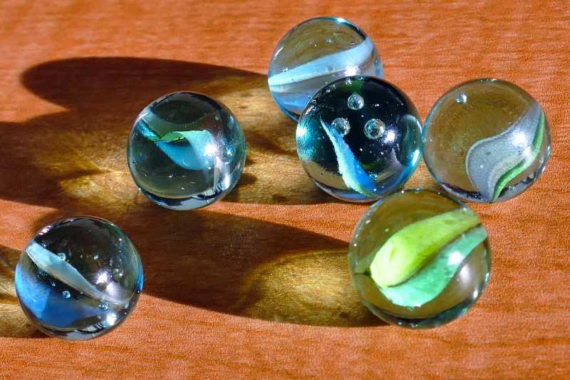 Six blue and green marbles on brown surface