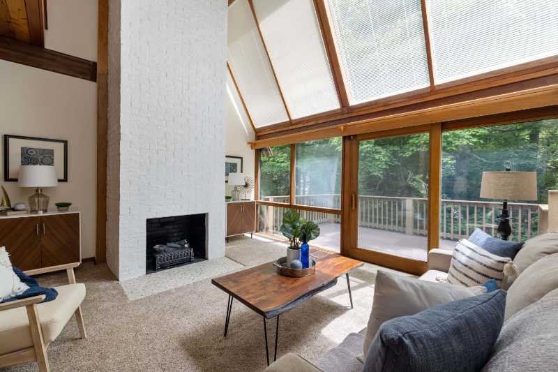 Spacious living room featuring a cozy fireplace and large windows overlooking forest greenery
