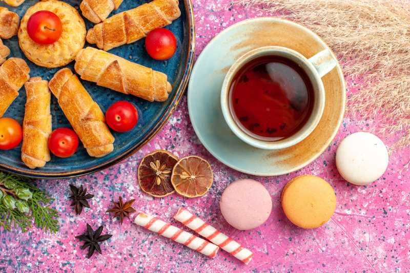 Sweet delicious bagels inside tray with fresh sour plums french macarons and cup of tea