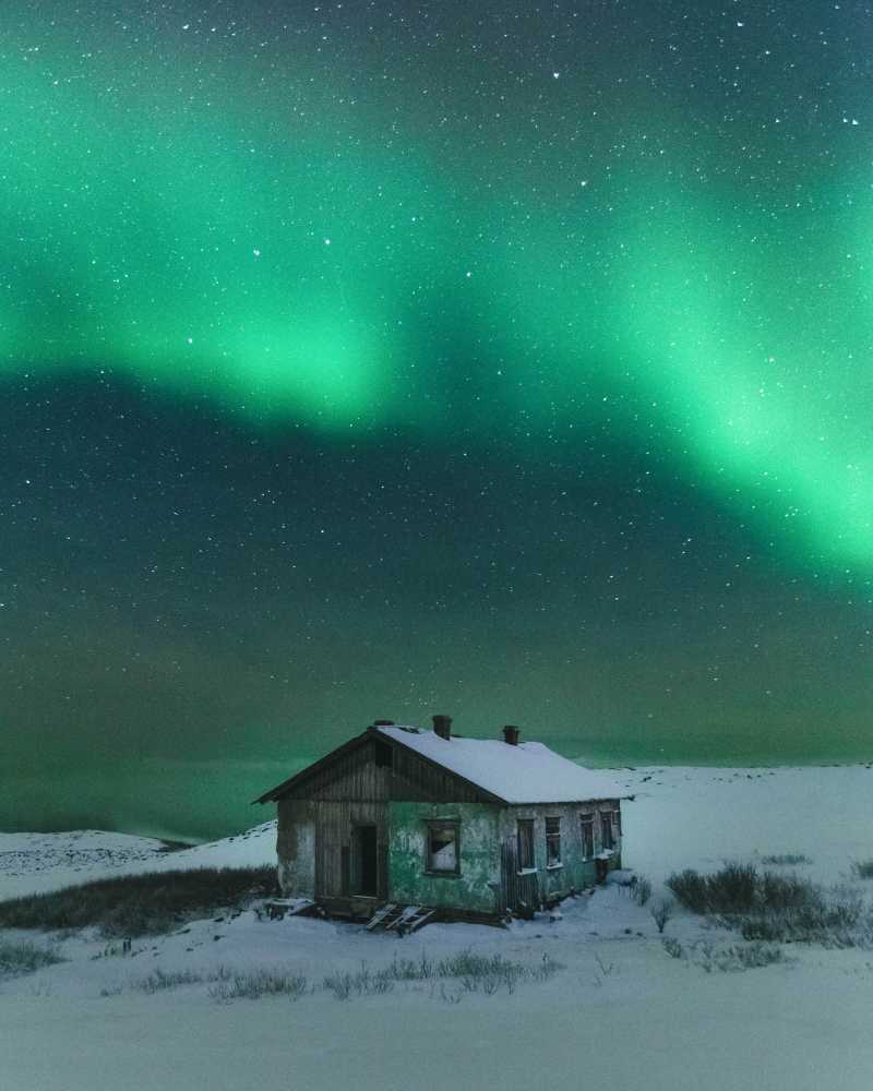 The Northern Lights in the sky over an abandoned building of weather station near Teriberka