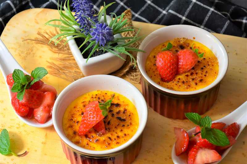 Dos porciones de postre de crema caramelizada con fresas frescas
