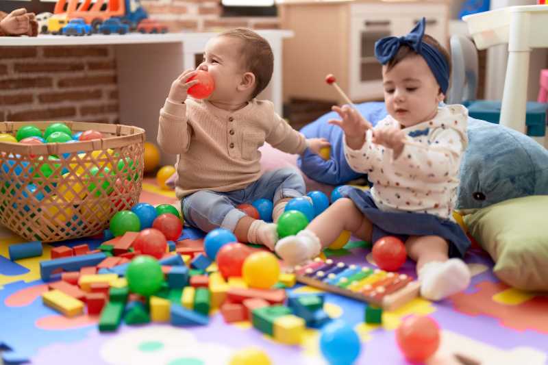 Deux tout-petits jouant avec des balles et un xylophone assis par terre à la maternelle