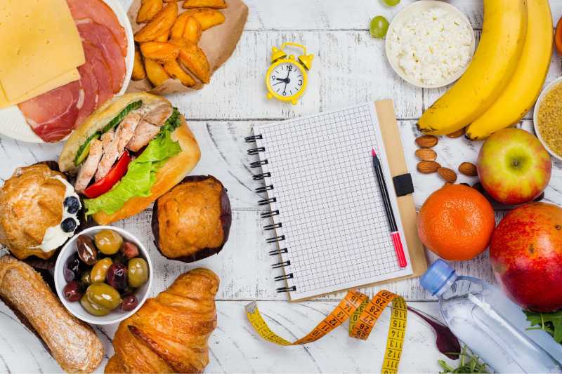 Variety of snacks fruits and savory foods surrounding a meal planner