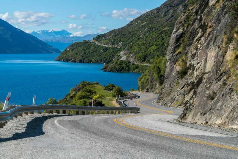 Carretera sinuosa a lo largo de un acantilado de montaña y un paisaje lacustre en Queenstown Nueva Zelanda. Viajes por carretera en verano en la Isla Sur.