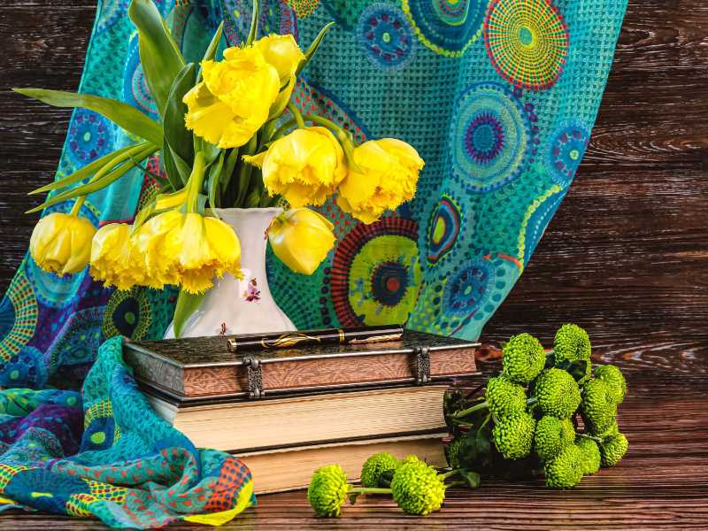 Yellow tulips in a vase with books and colorful fabric
